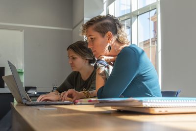 Two women work on laptops at a table.