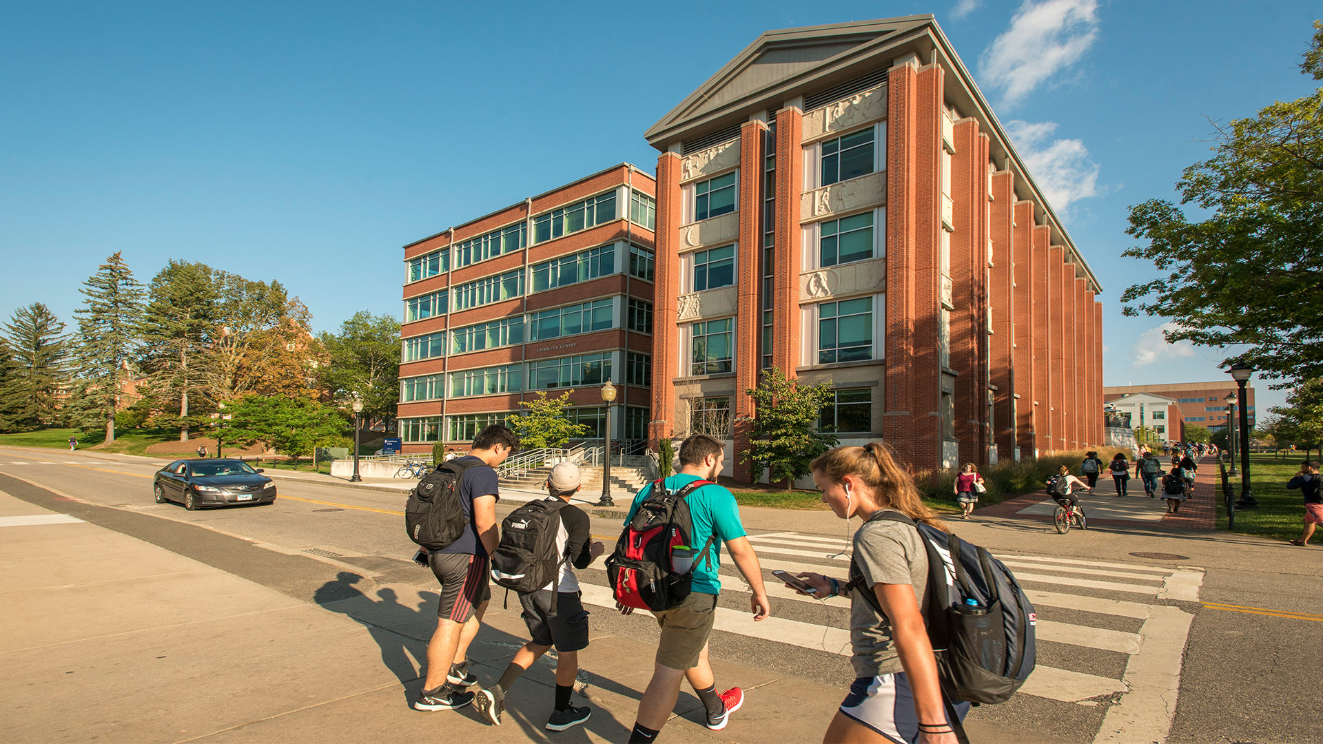 Students and a car pass by the Gentry Building in summer.